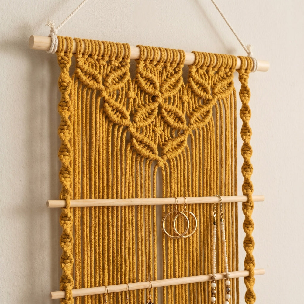 A mustard yellow macramé wall hanging featuring intricate woven patterns, wooden dowels, and space for jewelry storage.